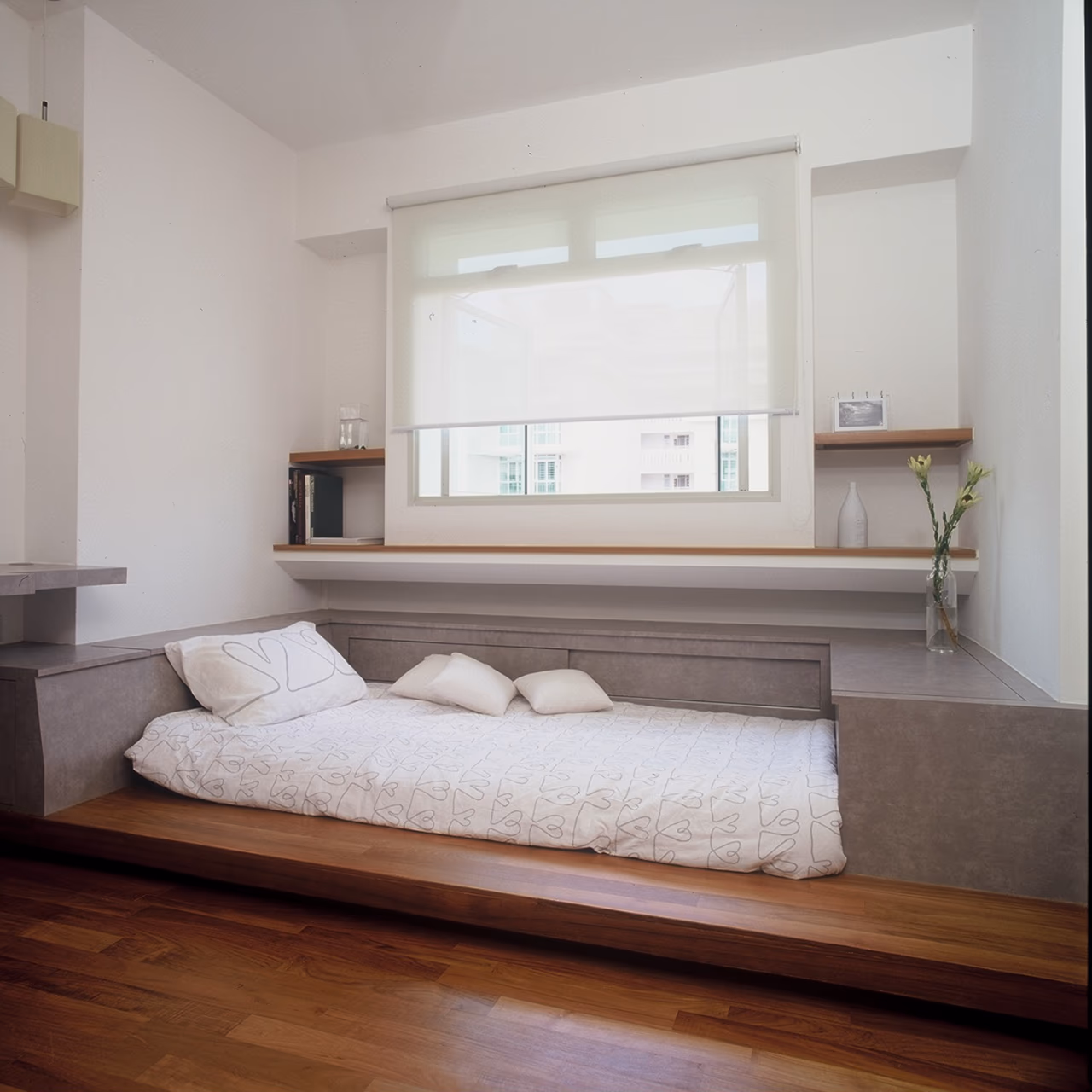 White roller blind half-lowered over a Singapore bedroom window above a platform bed