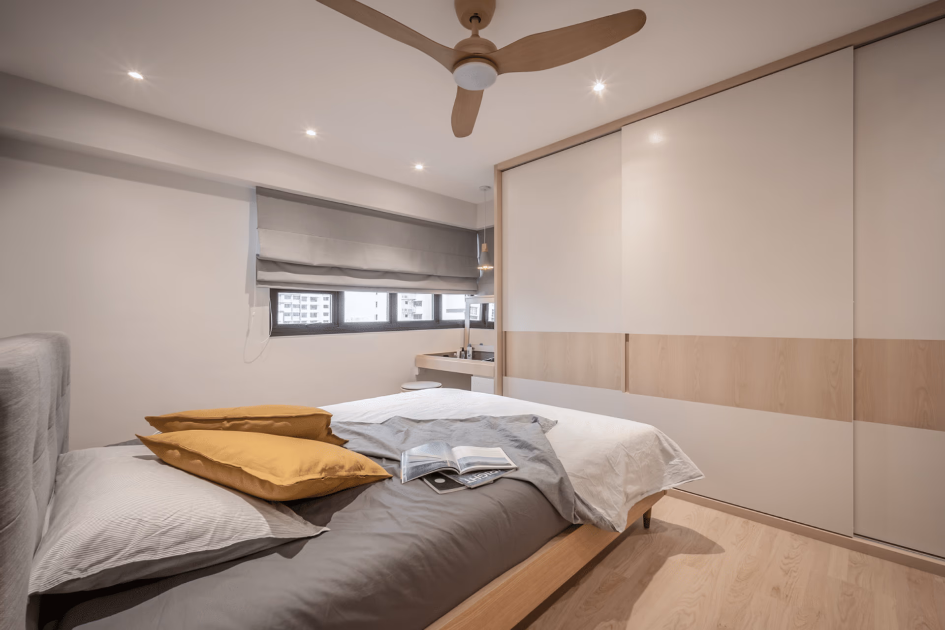 Grey Roman blind stacked above a Singapore bedroom window beside a light timber wardrobe