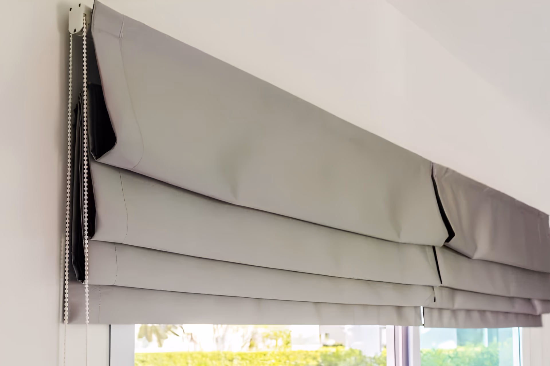 Grey Roman blind stacked in soft folds above a Singapore window, showing the neat pleat detail