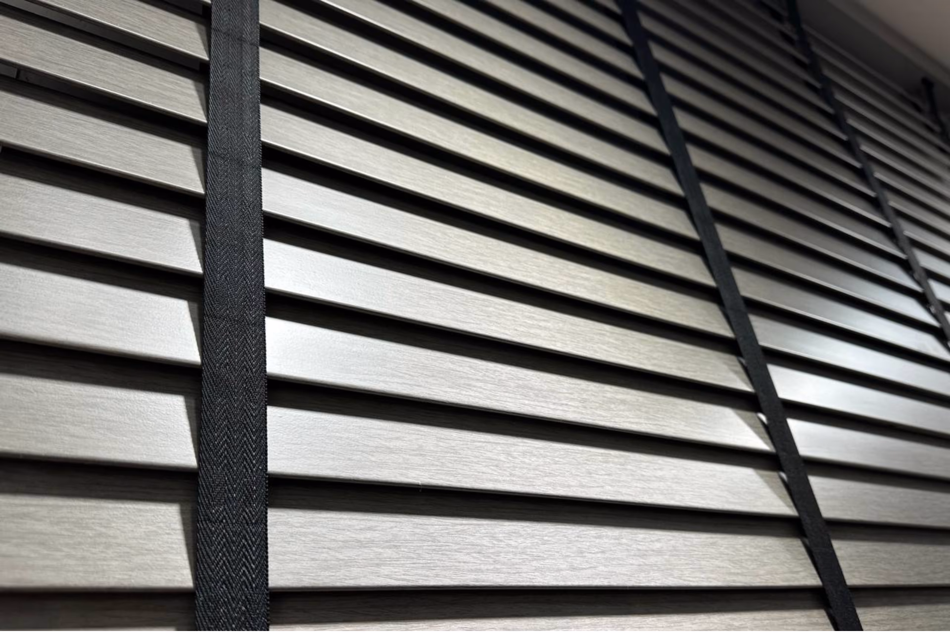 Close-up of light wood-grain Venetian blind slats with black ladder tape in a Singapore home