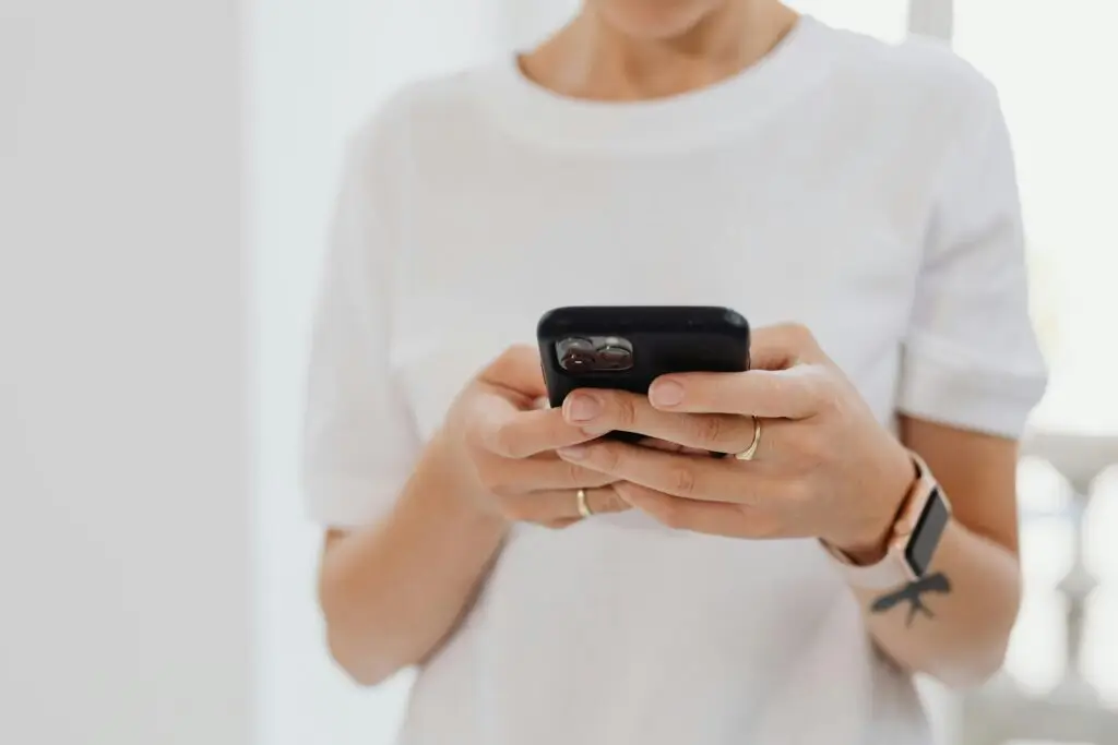 Adult using smartphone indoors, focusing on touchscreen communication.